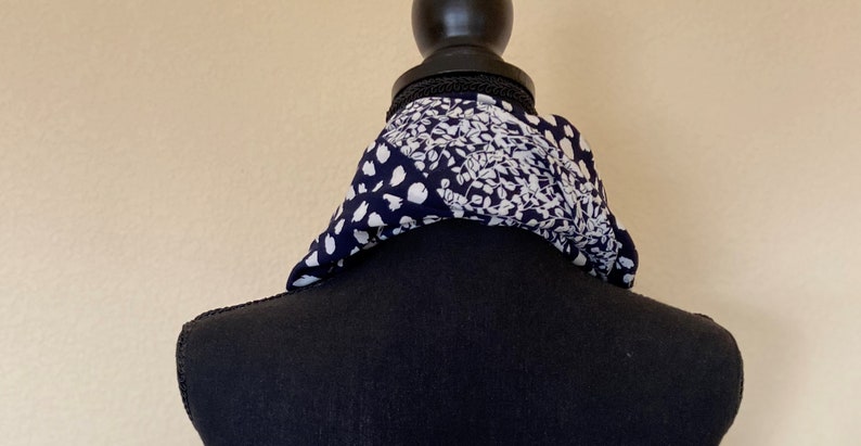 May include: A black and white patterned scarf with a floral design. The scarf is tied around a black mannequin's neck.