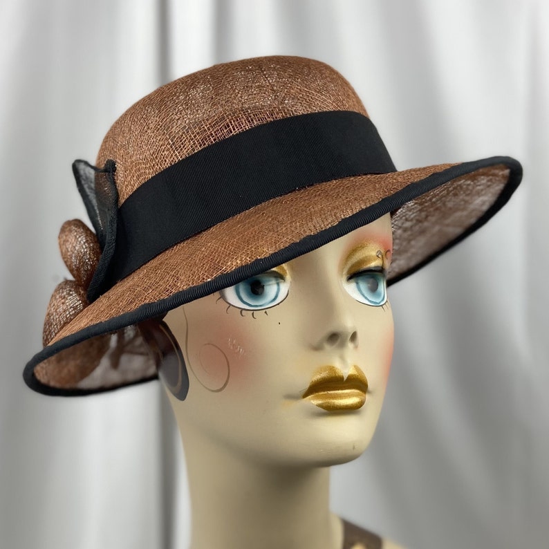Pu&ograve; includere: Un cappello di paglia marrone con un nastro nero e un bordo nero. Il cappello ha un'ampia tesa e una piccola corona.