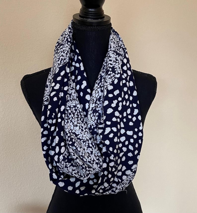 May include: A navy blue and white patterned infinity scarf. The scarf has a white floral pattern on one side and a white polka dot pattern on the other side.