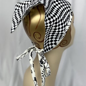 May include: A black and white checkered bandana with a floral patterned tie. The bandana is on a mannequin head. The tie is white with black floral designs. The bandana is made of fabric.