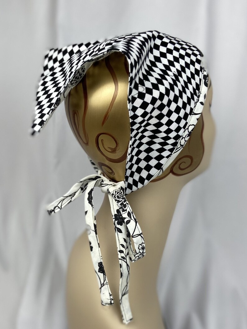May include: A black and white checkered bandana with a floral patterned tie. The bandana is on a mannequin head. The tie is white with black floral designs. The bandana is made of fabric.