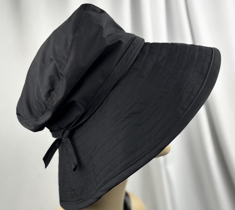 Pu&ograve; includere: Un cappello da sole nero con tesa larga e corona strutturata. Il cappello presenta un dettaglio a fiocco sul lato ed &egrave; realizzato in un tessuto liscio e opaco. La tesa ha un design trapuntato cucito.