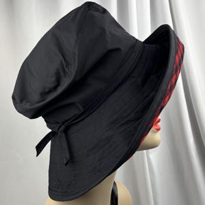 Pu&ograve; includere: Cappello a secchiello nero con interno a quadri rossi e neri. Il cappello ha un'ampia tesa e un dettaglio a fiocco. Realizzato in tessuto resistente, adatto per l'uso all'aperto.