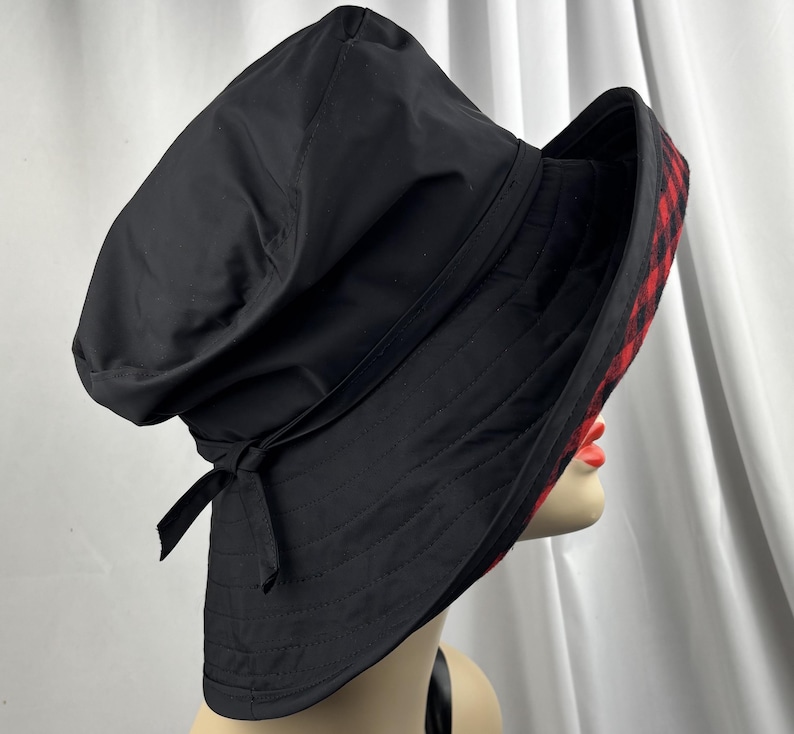 Pu&ograve; includere: Cappello a secchiello nero con interno a quadri rossi e neri. Il cappello ha un'ampia tesa e un dettaglio a fiocco. Realizzato in tessuto resistente, adatto per l'uso all'aperto.
