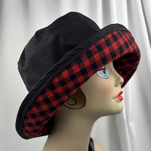 Pu&ograve; includere: Cappello da pescatore nero con bordo a quadri rossi e neri. Il cappello &egrave; realizzato in un materiale liscio. La tesa &egrave; ampia e il cappello ha uno stile classico e casual. L'interno della tesa presenta un motivo a quadri rossi e neri.