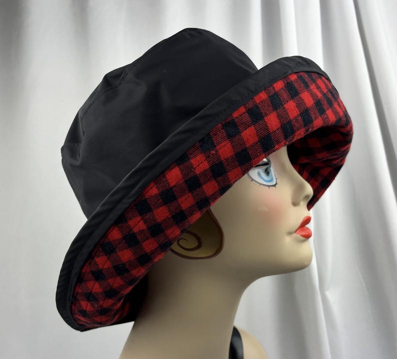 Pu&ograve; includere: Cappello da pescatore nero con bordo a quadri rossi e neri. Il cappello &egrave; realizzato in un materiale liscio. La tesa &egrave; ampia e il cappello ha uno stile classico e casual. L'interno della tesa presenta un motivo a quadri rossi e neri.