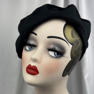 May include: A solid black beret made of a soft fabric material, featuring a rounded crown and a structured band that sits comfortably around the head. The hat has a smooth, matte texture and a classic, circular shape with no additional embellishments.
