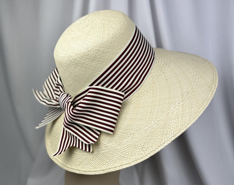 Pu&ograve; includere: Un cappello da sole color crema con una tesa larga e un nastro a righe nei toni del marrone e del bianco. Il nastro &egrave; annodato a fiocco sul lato del cappello, aggiungendo un tocco decorativo. Il cappello &egrave; realizzato in materiale tessuto.