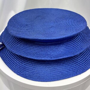 K&ouml;nnte beinhalten: Ein leuchtend k&ouml;nigsblauer Strohhut mit einer breiten, flachen Krempe und einer strukturierten, runden Krone. Der Hut besteht aus eng geflochtenem Strohmaterial und verf&uuml;gt &uuml;ber ein kleines, passendes blaues Band an der Seite der Krempe.