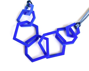 Può includere: Una collana caratterizzata da una serie di esagoni geometrici blu vibrante interconnessi, realizzati in materiale liscio. Gli esagoni sono collegati tra loro in un motivo a cascata e sono sospesi a un cordino blu scuro che passa nella parte superiore.