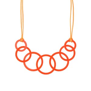 May include: A vibrant orange necklace featuring a series of interconnected circular links. The necklace is suspended by a thin, orange cord. The design is modern and minimalist, with a focus on geometric shapes and bold color.