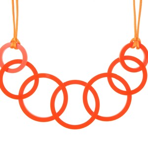 May include: A necklace featuring a series of interlocking orange rings. The necklace is suspended from an orange cord. The rings are a vibrant orange color, and the cord is a lighter orange. The necklace is a modern and minimalist design.