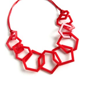 May include: A necklace featuring a series of interconnected bright red hexagonal frames of varying sizes. The geometric shapes are linked together to form a chain, suspended from a thin red cord that extends from both ends of the arrangement.