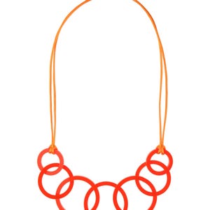 May include: A modern necklace featuring six vibrant red circular pendants connected by an orange cord. The cord is secured with a silver-colored magnetic clasp. The necklace is a bold statement piece.