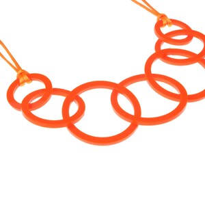 May include: An orange necklace featuring a series of interconnected circular links. The necklace is suspended from a thin orange cord. The design is modern and minimalist, with a focus on geometric shapes and bright color.
