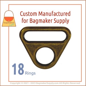 May include: A set of 18 antique brass D-rings, each with a triangular shape and a round hole. The rings are designed for use in crafting and bag making.