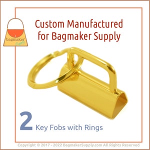 May include: Two gold-colored key fobs with rings. The key fobs are made of metal and have a rectangular shape. The rings are attached to the key fobs with a small loop.