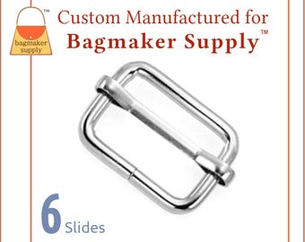 Könnte beinhalten: Silberner Metall-Schieberverschluss für Riemen oder Taschen. Die Schnalle ist rechteckig mit abgerundeten Ecken und hat eine glatte Oberfläche. Der Text "Custom Manufactured for Bagmaker Supply" ist über der Schnalle sichtbar.