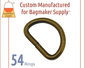 以下が含まれることがあります： アンティークブラス製のDリング54個のクローズアップ。リングはBagmaker Supplyのためにカスタムメイドされています。