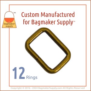 May include: A pack of 12 gold-toned metal rings, each with a rectangular shape. The rings are designed for use in crafting and bag making. The image includes the text "Custom Manufactured for Bagmaker Supply™".