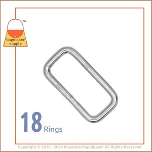 May include: A pack of 18 silver metal rings. The rings are rectangular in shape and have a smooth finish. They are commonly used for attaching straps or handles to bags or other projects.
