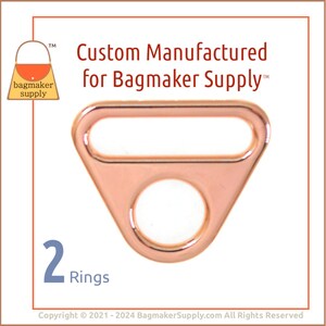 May include: Two rose gold metal rings with a triangular shape and a round opening. The rings are designed for use in bag making.