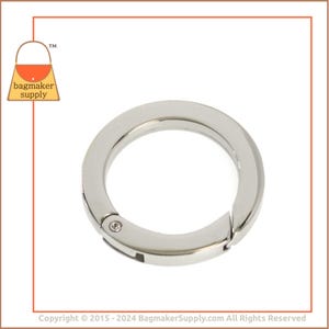 Könnte beinhalten: Silberner Drehverschlussring zum Anbringen an Taschen, Geldbörsen oder anderen Accessoires. Der Ring ist aus Metall und hat eine glatte, polierte Oberfläche.
