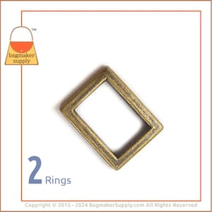 May include: Two antique gold metal rings, each with a rectangular shape. The rings are ideal for attaching to straps or other leather goods.