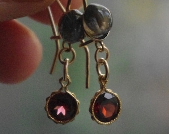 May include: Gold earrings with a dark gray stone and a red gemstone. The earrings have a drop design.