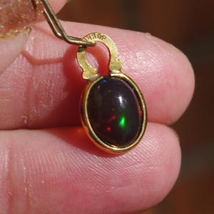 Peut inclure: Un pendentif en or avec une pierre d'opale ovale foncée. L'opale présente un reflet vert et rouge.