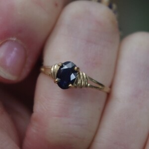 May include: A gold ring with a dark blue oval gemstone set in a wire-wrapped design.