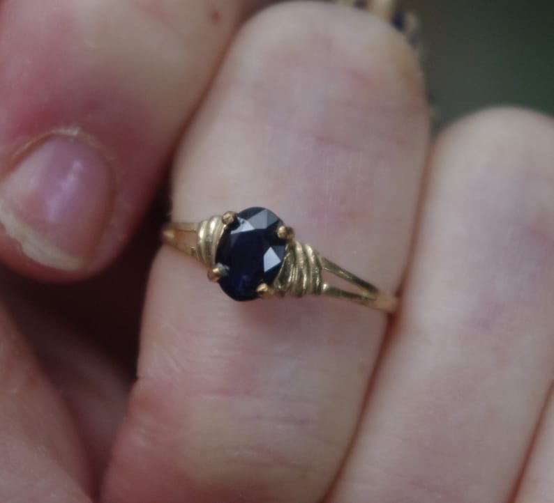 May include: A gold ring with a dark blue oval gemstone set in a wire-wrapped design.