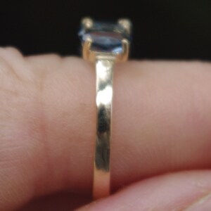 Puede incluir: Un anillo de banda de oro con una piedra preciosa azul engastada en el centro.