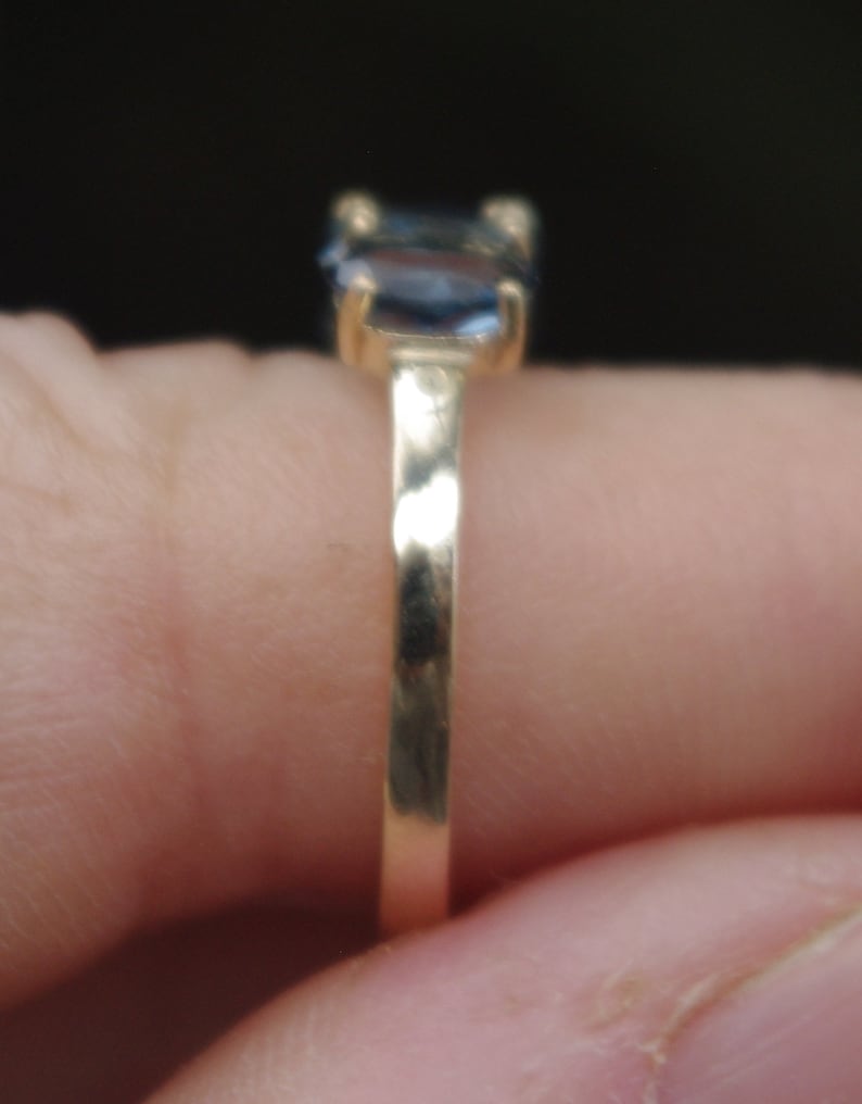 Puede incluir: Un anillo de banda de oro con una piedra preciosa azul engastada en el centro.