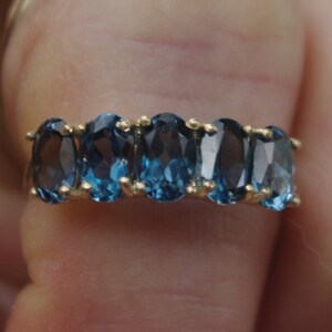 Puede incluir: Un anillo de banda de oro con una fila de piedras azules ovaladas.