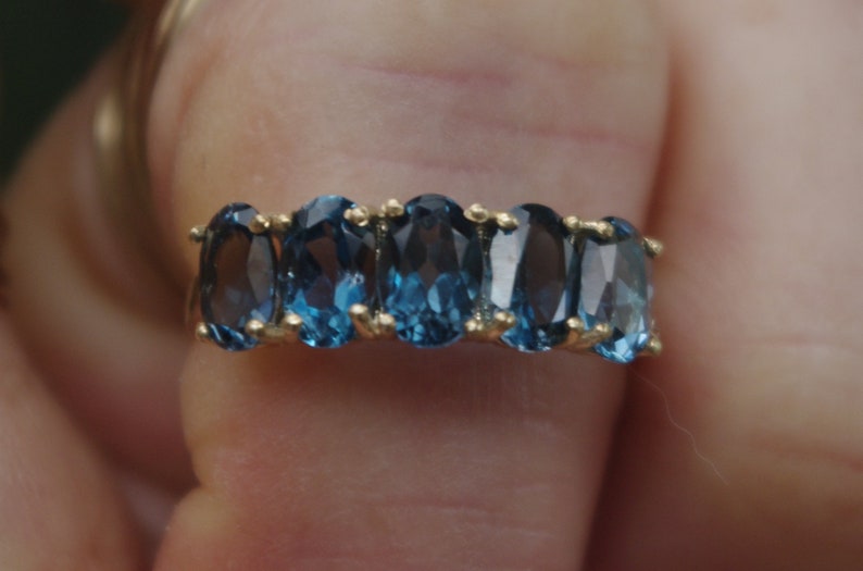 Puede incluir: Un anillo de banda de oro con una fila de piedras azules ovaladas.
