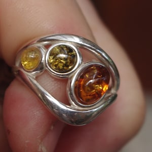 May include: A silver ring with three amber stones set in a swirl design.