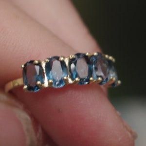 Puede incluir: Un anillo de banda de oro con seis piedras preciosas azules ovaladas.