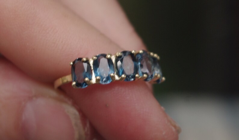 Puede incluir: Un anillo de banda de oro con seis piedras preciosas azules ovaladas.