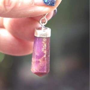 May include: A silver pendant with a purple and gold crystal point.