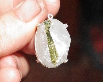 May include: A silver pendant featuring a clear quartz crystal with a green inclusion. The pendant is oval shaped and has a silver bail.