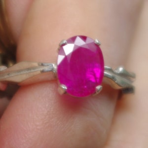 May include: A silver ring featuring a large oval pink ruby gemstone.
