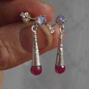 May include: A pair of silver dangle earrings with a small purple gemstone at the top and a larger pink gemstone at the bottom.