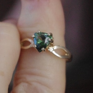 Puede incluir: Un anillo de oro con una piedra preciosa verde engastada en forma de triángulo.