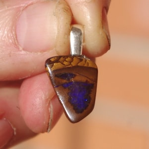 May include: A pendant with a silver bail, featuring a polished, teardrop-shaped opal. The opal displays a mosaic of colors, including brown, gold, and a vibrant blue, creating a unique and eye-catching design. Jewelry.