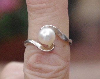 May include: A silver ring with a white pearl set in a wave-like design.