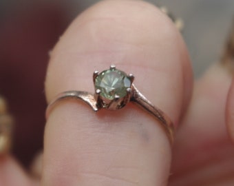 May include: A silver ring with a green gemstone set in a prong setting. The ring has a simple band and a delicate design.