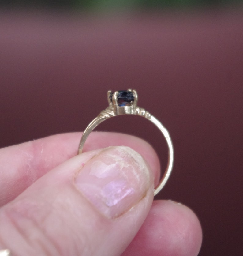 May include: A gold ring with a dark blue gemstone set in a simple, elegant design.
