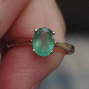 Puede incluir: Un anillo de oro con una gran piedra preciosa ovalada de color verde esmeralda.