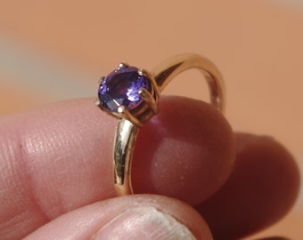 Puede incluir: Un anillo de oro con una piedra preciosa púrpura engastada en garras.